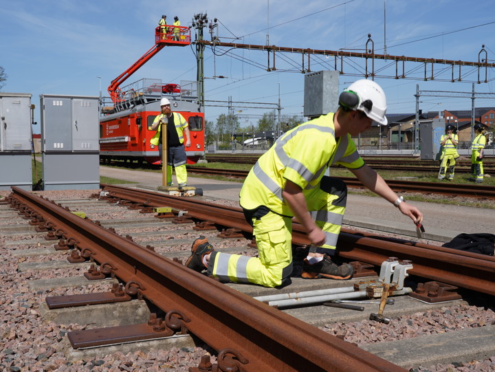 Utbildning pågår i Trafikverksskolans övningspark för järnväg med flera personer i varselkläder som övar i spårväxlar och underhåller kontaktledning på hög höjs från korgen till en lifträlsbuss.